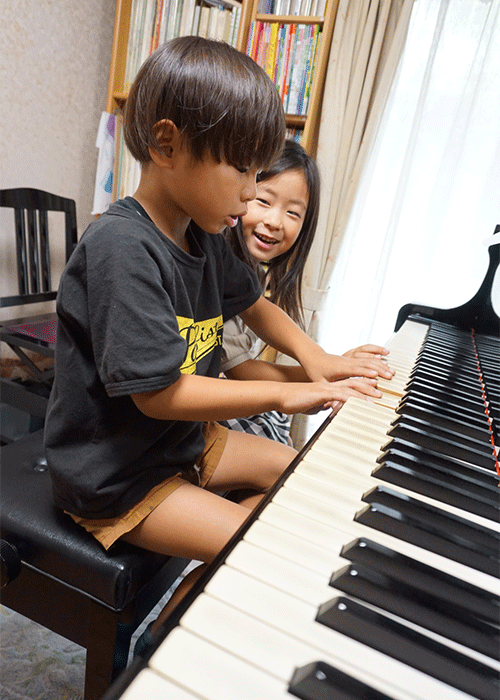 2人でピアノを弾く笑顔の子供の写真