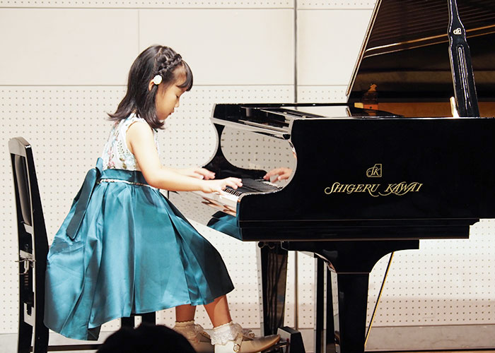 水色のスカートの衣装の女の子のピアノ発表の写真